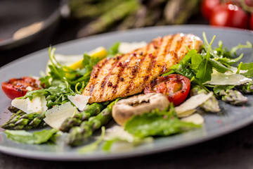Grilled chicken breast asparagus arugula mushrooms tomatoes lemon and parmesan cheese.