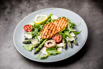 Grilled chicken breast asparagus arugula mushrooms tomatoes lemon and parmesan cheese.