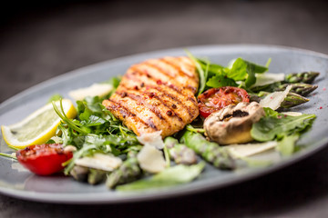 Grilled chicken breast asparagus arugula mushrooms tomatoes lemon and parmesan cheese.