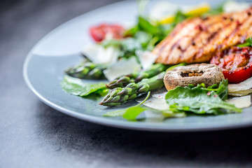 Grilled chicken breast asparagus arugula mushrooms tomatoes lemon and parmesan cheese.