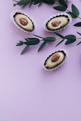 Flat lay of delicious praline sweets with almonds on purple background with green spring twigs