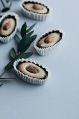 Composition of delicious praline sweets with almonds and green twigs on blue background