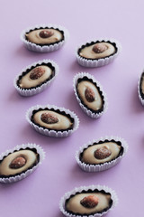 Flat lay of delicious praline sweets with almonds on purple background