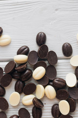Flat lay of delicious sweet chocolate drops on white wooden background
