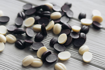 Flat lay of delicious sweet chocolate drops on white wooden background