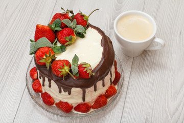 Homemade chocolate cake decorated with fresh strawberries on glass plate and cup of coffee