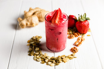 A strawberry ginger smoothie cocktail in a highball glass, garnished with fresh berries, ginger, walnuts and pumpkin seeds. White wooden table.