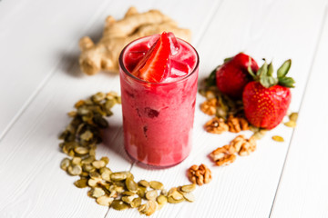 A strawberry ginger smoothie cocktail in a highball glass, garnished with fresh berries, ginger, walnuts and pumpkin seeds. White wooden table.