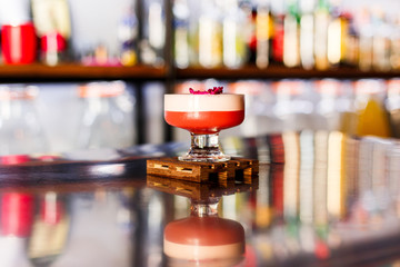 A lifestyle photo of a clover club alcoholic drink in a cocktail glass, served on a small wooden board, standing on a steel barstand. Selective focus, grain effect, bokeh background.