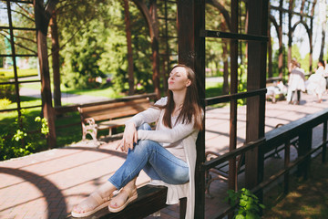Obraz premium Portrait of beautiful caucasian young woman with charming smile wearing light casual clothes. Smiling female sitting under archway in city park in street outdoors on spring nature. Lifestyle concept.