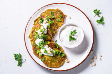 Zucchini pancakes with greens and sour cream on white.