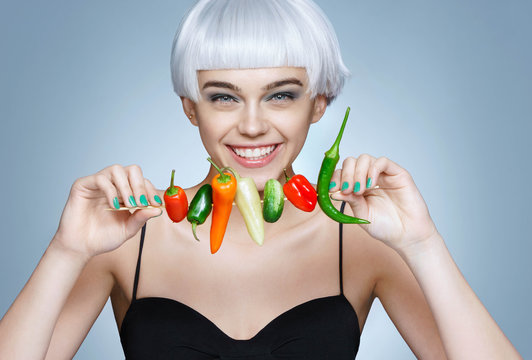 Beautiful young girl with different peppers. Photo of smiling blonde girl with flawless skin on blue background. Healthy lifestyle