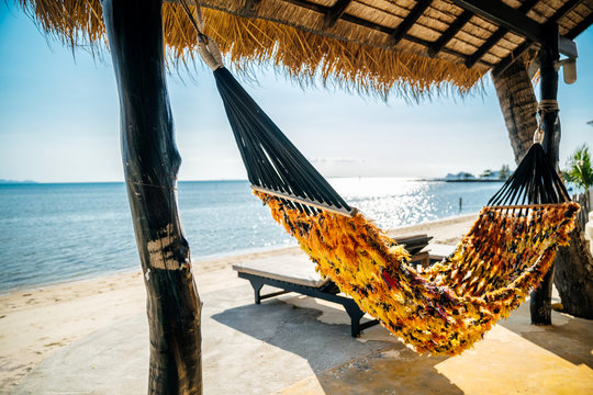 Yellow hammock on the background of a sea landscape under the roof of an exotic bungalow. Summer mood and travel.