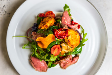 A warm salad with roastbeef, arugula, cherry tomatoes, dried carrot and grilled cheese.