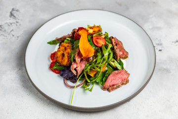 A warm salad with roastbeef, arugula, cherry tomatoes, dried carrot and grilled cheese.