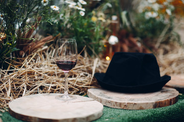 Glass of wine and hat on table decorated with hay in rustic style
