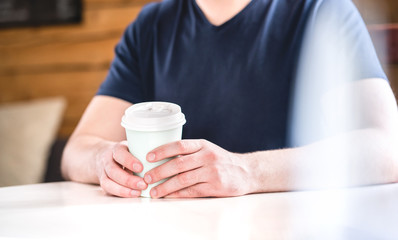 Man holding take away coffee cup in hands on table in cafe, coffee shop or home. Guy with hot chocolate or tea.