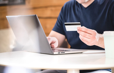 Man holding credit card and typing bank information or identification numbers with laptop. Ecommerce and online shopping concept.
