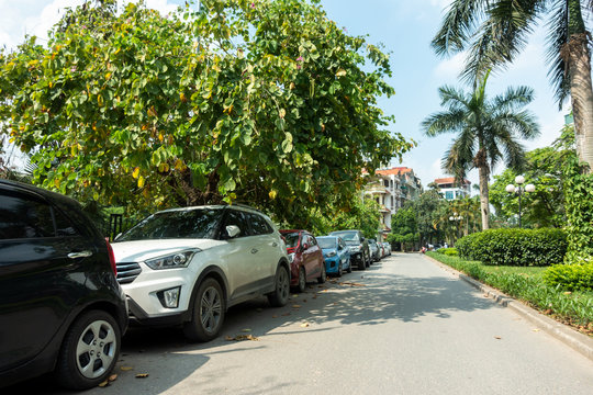 Parallel cars parking on street with green trees