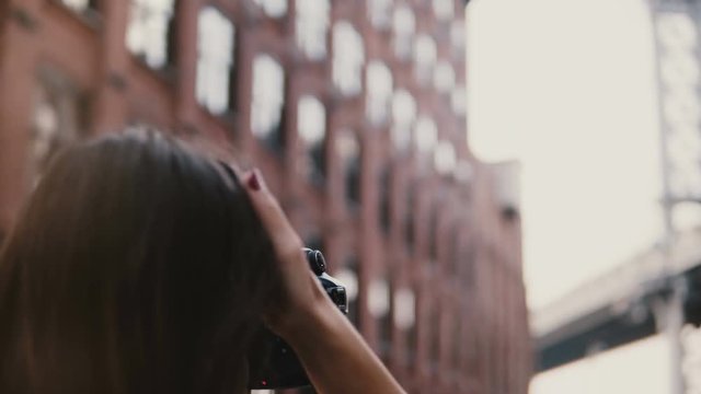 Back view professional female photographer with camera takes pictures of Brooklyn Bridge at Dumbo District, New York 4K.