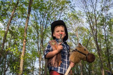 Portrait a little boy dressed like a cowboy with toy horse and pistol on outdoors. Costume party