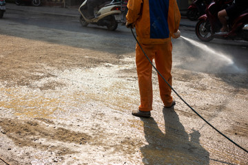 Worker making street wet with water spray at construction area