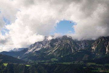 Paraglider flying over Schladming town with Dachstein mountains background, Northern Limestone Alps, Austria, dramatic cloudy sky