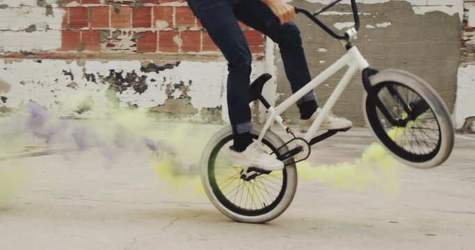 Close up of extreme BMX biker doing tail whip trick with purple and yellow colored smoke grenade  in urban environment