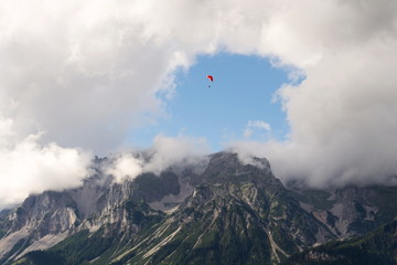 Paraglider flying over Schladming town with Dachstein mountains background, Northern Limestone Alps, Austria, dramatic cloudy sky