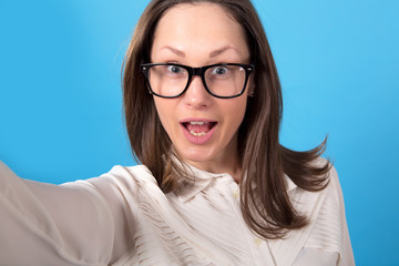 Obraz premium Young woman in glasses makes a selfie portrait on a blue background.