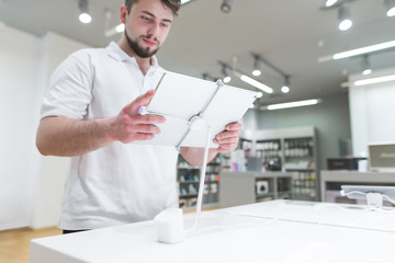 Smiling bearded man chooses a tablet in the electronics store. A man with a tablet in his hands against the background of a bastard store. Gadget selection. Focus on the tablet.