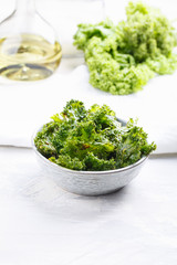 Kale chips in bowl. Crispy green kale chips dehydrated with salt, oil and vegan cheese. Healthy homemade vegan snack.
