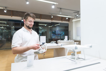 Happy man is in the technology store with a controller for a drone in his hands and smiles. Dron test in a quadcopter store.