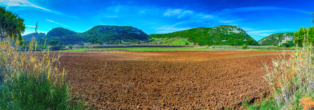 Beautiful panoramic pastoral, surrounded by evergreen trees on steep hills. Farm fields of red soil in the valley of the Alcabrichel river. A typical agricultural landscape near Vimeiro in Portugal.
