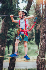 Little boy climbing in adventure activity park with helmet and safety equipment