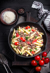 Pasta with tomatoes and meat on  dark rustic background.