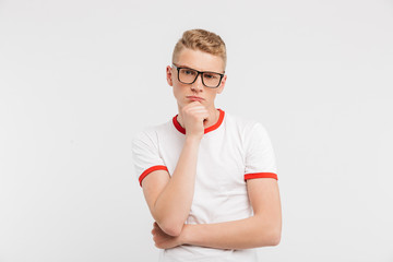 Image of smart serious guy wearing eyeglasses looking at camera with brooding gaze and touching chin, isolated over white background