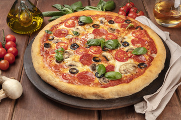 Pepperoni pizza on a pizza stoen, with white wine and ingredients