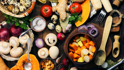 cut mushrooms, pumpkin and potatoes in a clay pot. cooking healthy food. spices and ingredients. wooden background.