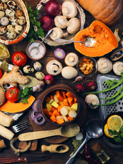 cut mushrooms, pumpkin and potatoes in a clay pot. cooking healthy food. spices and ingredients. wooden background.