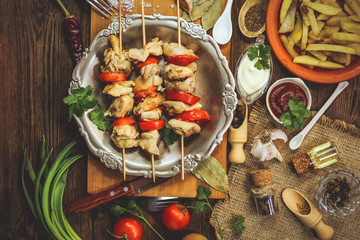 fried chicken meat with tomatoes on wooden sticks. Barbecue with vegetables on a wooden background.