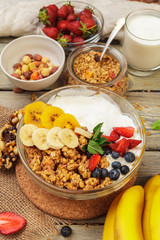Bowl of homemade granola with yogurt and fresh berries on wooden background