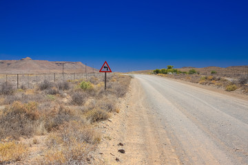 Desert landscape view of a sharp left turn sign on a dirt road in the Karoo of South Africa