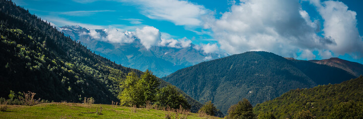 Fototapeta na wymiar Amazing panoramic view to Caucasus Mountains. Densely coniferous forests and high snowed mountain peaks. Sunny day with blue mountains. Svaneti, Geogria.