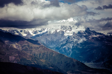 Fototapeta na wymiar Amazing view to Caucasus Mountains. Adorable high mountain peaks in .thick and dark cumulus clouds. .Village in the mountain valley. Svaneti, Geogria.