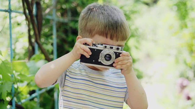 Portrait of a lovely little boy taking photos outdoors on the vintage camera and than looking into the camera and smile