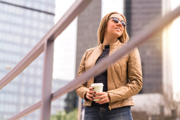 Happy relaxed woman enjoying take away cup of coffee in city street. Lady having coffee break in downtown. Tourist or business person having peaceful moment with beverage. Urban lifestyle.