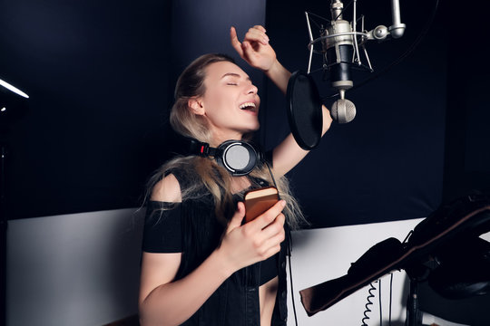 Create something new! Side view portrait of the attractive young woman music artist with mobile phone recording a song in the music studio.