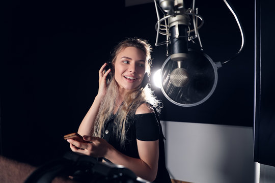 Create your music! Beautiful young girl smiling, while reading lyrics and singing a song with a mobile phone in the recording studio.