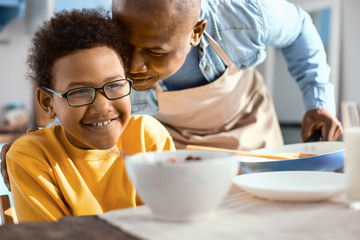 Love you. Gentle young father whispering affectionately at his little sons ear while the boy having breakfast in the kitchen